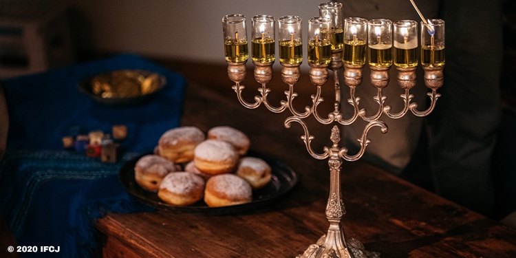 A lit menorah with donuts and other treats behind it.