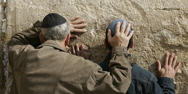 A man and young boy pray to the Western Wall in Jerusalem with their heads pressed against the wall