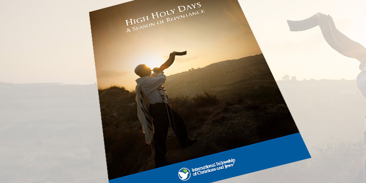 A person raising their hand in prayer during sunset on a hill, symbolizing spiritual reflection and renewal for High Holy Days.