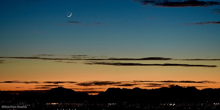 An orange and blue sunset with a lit-up city below it.