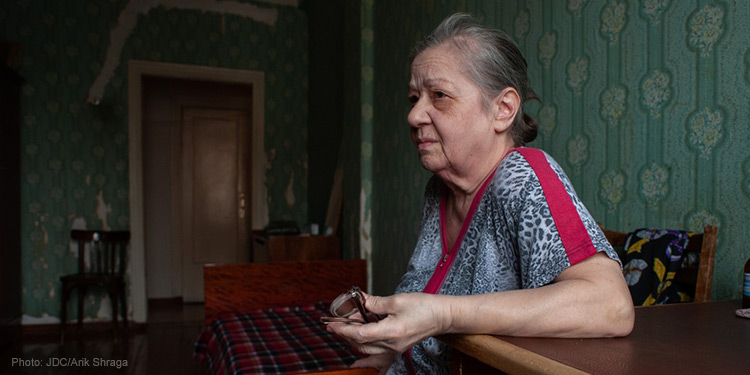 elderly woman sitting down, elbow resting on desk