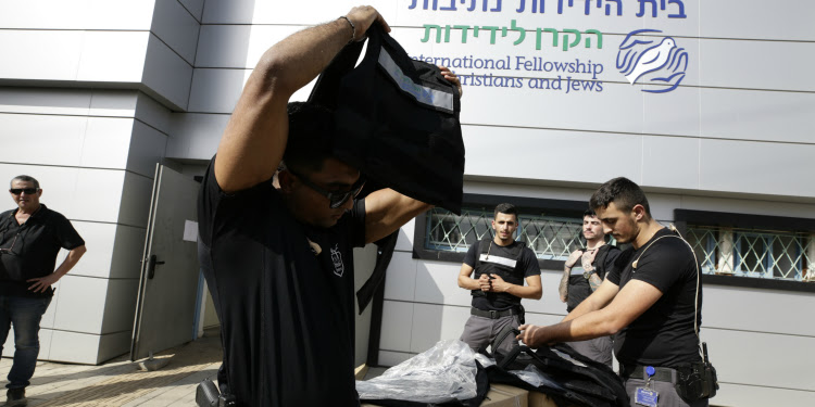 Man putting a vest on alongside others outside the IFCJ building.