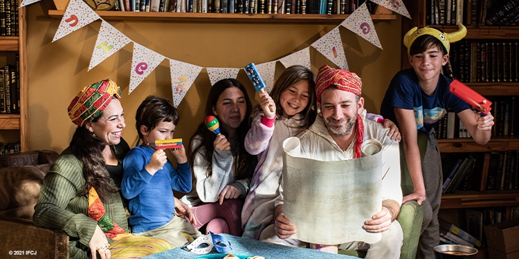 Yael Eckstein and her family celebrating Purim with costumes, decorations, and cookies, Yael and Ami with their children Meyora, Liam, Sapir, and Shimmy, hamantaschen, maracas, toys, candy, scroll, smile
