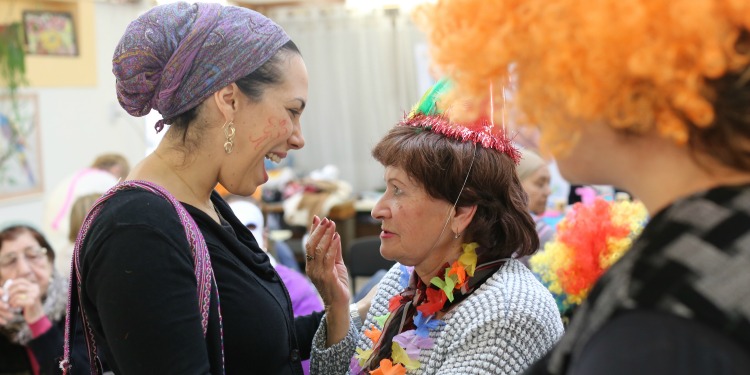 Yael Eckstein smiling at an elderly woman while at a Purim party.