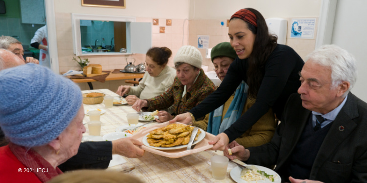 Yael Eckstein passing a plate while Holocaust survivors have dinner together.