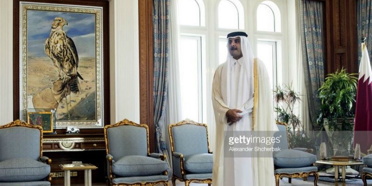 Man in a robe standing inside a luxurious room with several chairs, an eagle painting, and a large window.