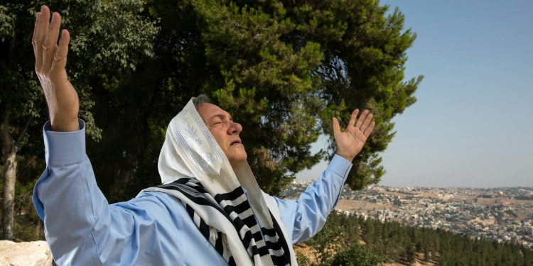 Rabbi Yechiel Eckstein stands on a hillside praying with his hands stretched toward the sky