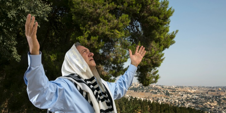 Rabbi Yechiel Eckstein stands on a hillside praying with his hands stretched toward the sky