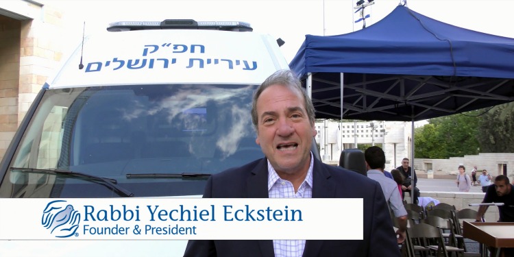 Rabbi Eckstein in a suit standing in front of an IFCJ branded van.