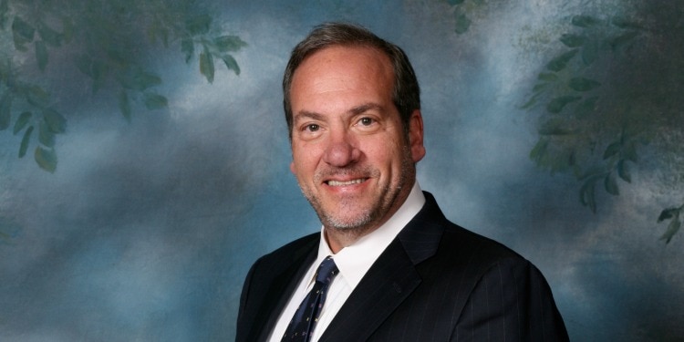 Rabbi Eckstein smiling as a blue background with green leaves is behind him.