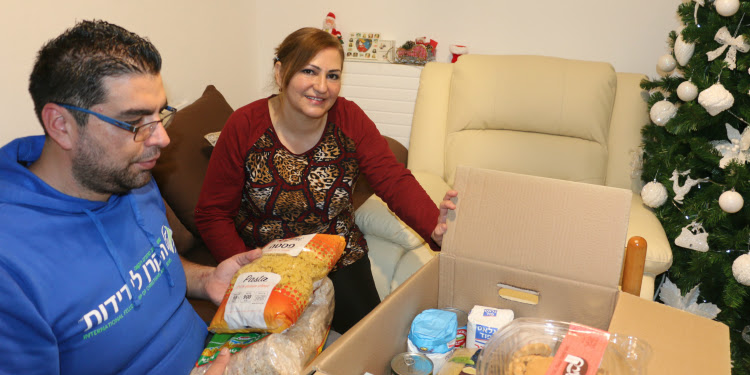 Man wearing an IFCJ sweatshirt helping a woman unbox her IFCJ food box.