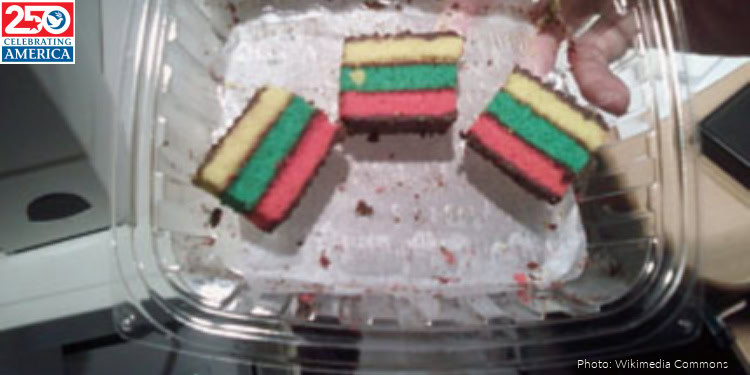 Colorful rainbow layered cake slices on a clear plastic tray, showcasing vibrant red, yellow, and green layers, perfect for celebrations and festive occasions.