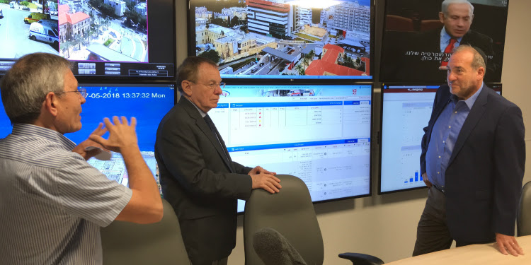 Rabbi Eckstein talking with two other men in a conference room with TVs.