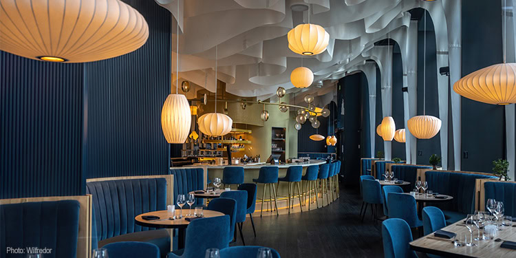 Stylish restaurant interior featuring blue seating, hanging pendant lights, and a curved bar area, creating a sophisticated dining atmosphere.