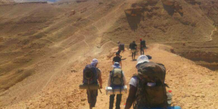 Soldiers hiking up a desert mountain with backpacks.