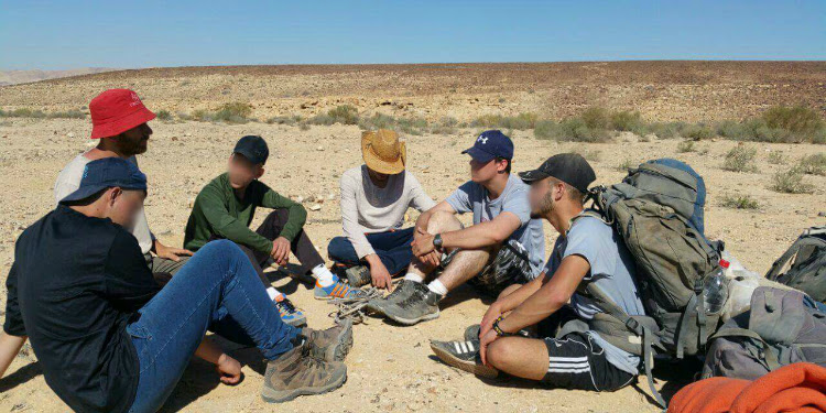 Six young men sitting on the ground in a middle of a hike.