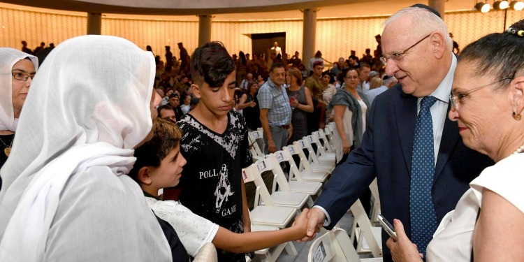President Rivlin shaking hands with a young boy who's standing with his family at a conference.