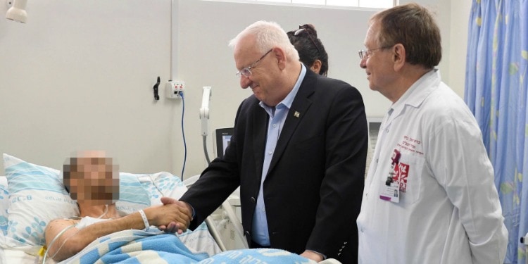 Elderly man shaking hands with a hospital patient laying in bed.