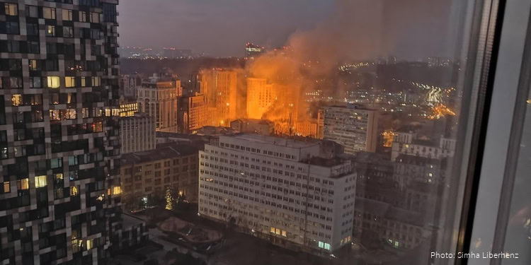 Large fire with thick smoke rising over Kyiv cityscape during night, buildings illuminated by flames and city lights in the background.