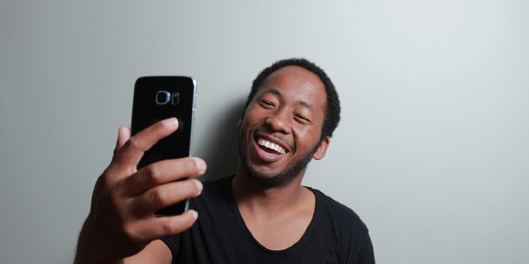 Man smiling at his cell phone while he takes a selfie.