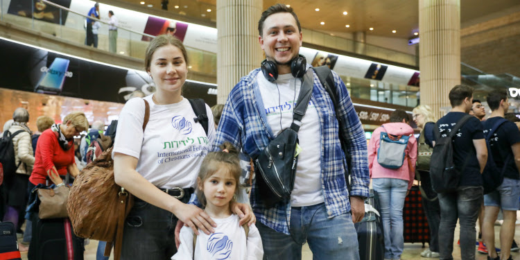 Alexander and Mariia Pecherskii with their daughter wearing IFCJ shirts in the airport.