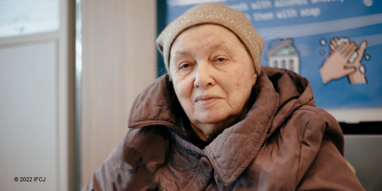Elderly Jewish woman in a brown jacket looking directly into the camera.