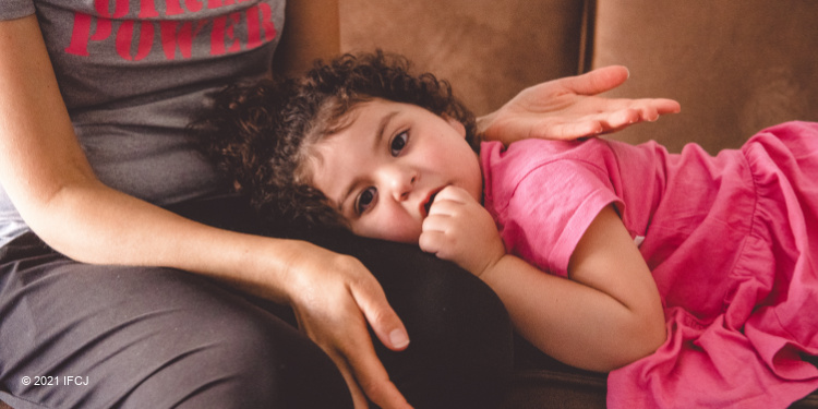 Little girl laying on the lap of her mother while looking directly into the camera.