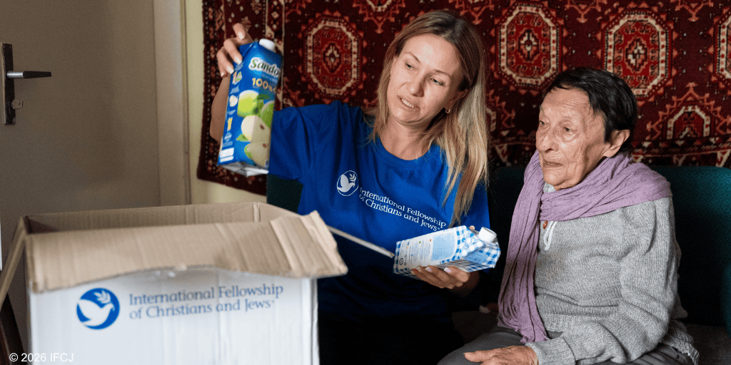A volunteer from IFCJ hands a box of supplies to an elderly woman, demonstrating compassion and support for those in need.