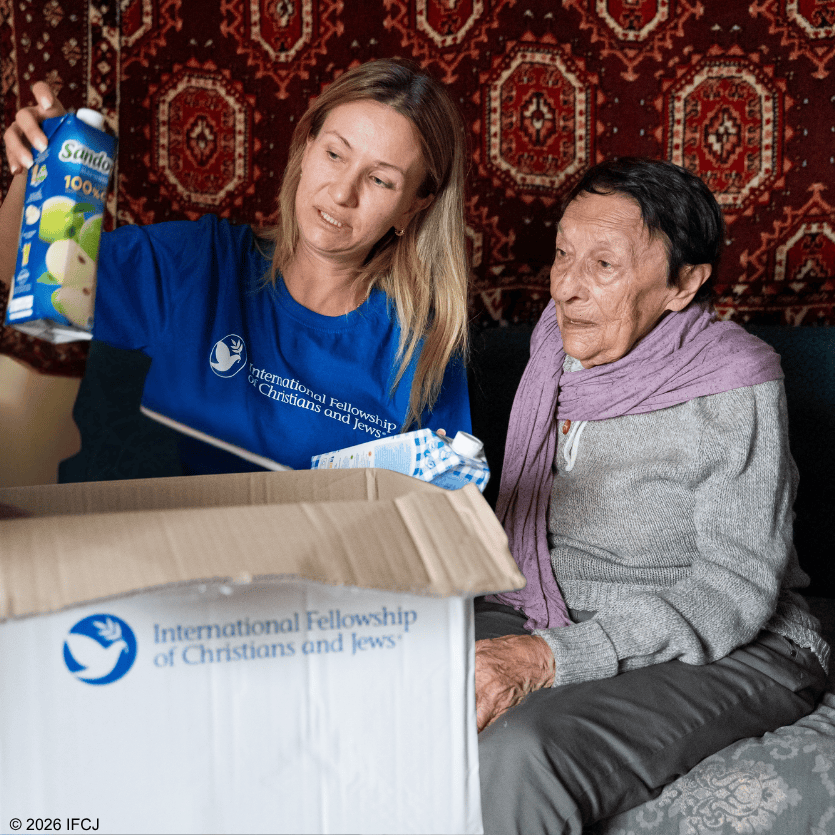 A volunteer from IFCJ hands a box of supplies to an elderly woman, demonstrating compassion and support for those in need.