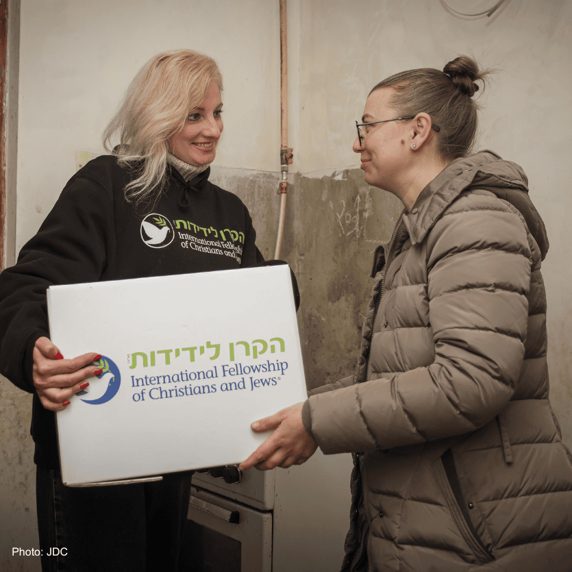 blonde woman, black branded logo sweatshirt - delivering branded logo food box - handing food box to woman with glasses, tan puffer coat - smiling