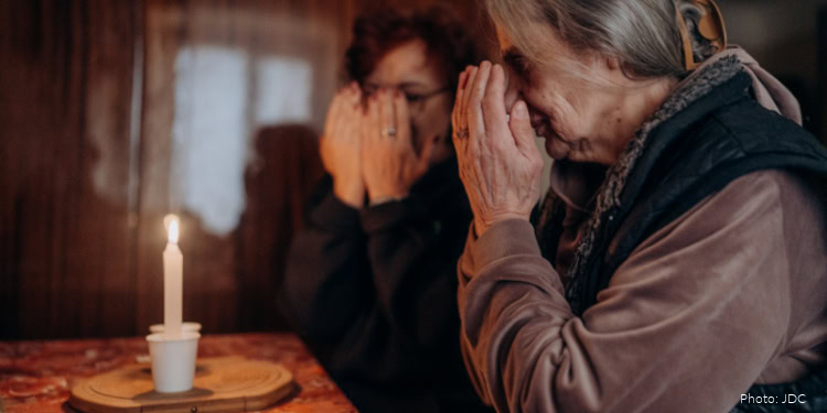 Two women praying with hands covering their faces during Shemini Atzeret celebration, reflecting devotion and spiritual reflection.