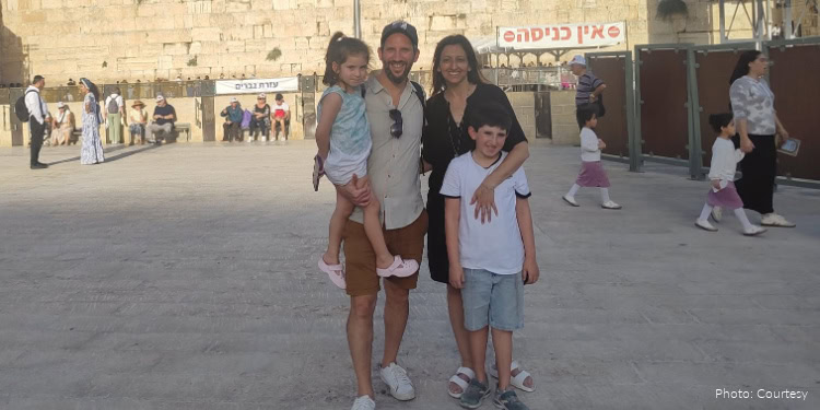 Happy family with two children visiting Jerusalem, Israel, enjoying a day outdoors near the Western Wall with other visitors in the background.