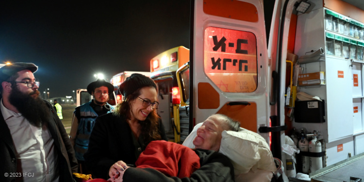 Yael Eckstein holding the hand of an elderly woman exiting an ambulance van.