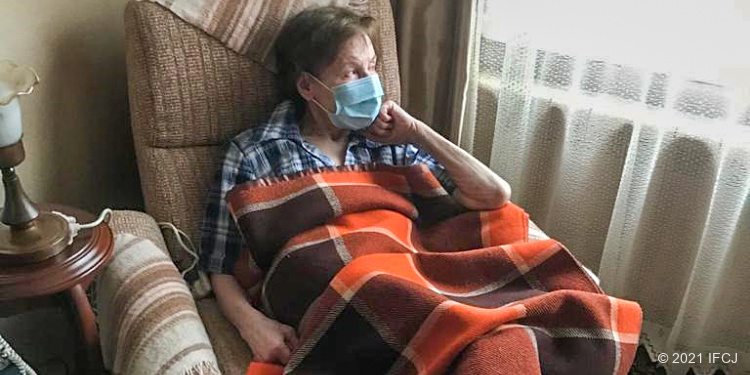 Elderly woman sitting in a chair under a plaid blanket and wearing mask