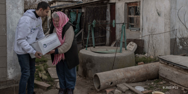 IFCJ employee handing a lifesaving box of food to a elderly woman.