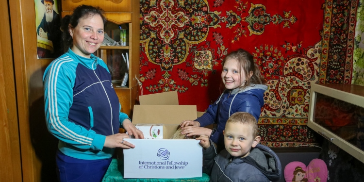 Ksenia and family smiling while holding an IFCJ food box.