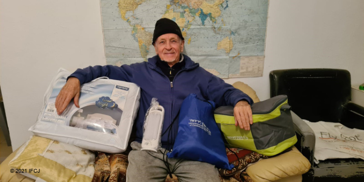 Elderly Jewish man sitting with gifts given to him from IFCJ.