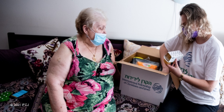 Elderly Jewish woman looking through IFCJ food box with an IFCJ volunteer.