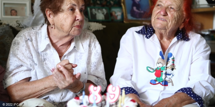 Two elderly Jewish women in white shirts sitting next to eachother.