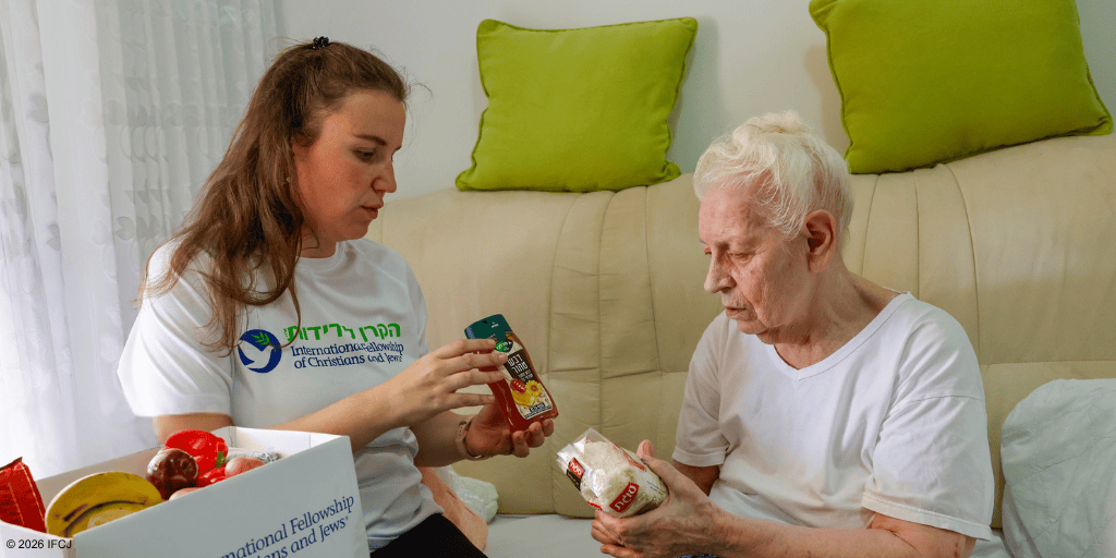 Young woman providing food and support to an elderly woman in a cozy living room setting, highlighting kindness and community support.