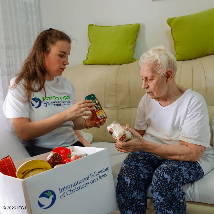 Young woman providing food and support to an elderly woman in a cozy living room setting, highlighting kindness and community support.