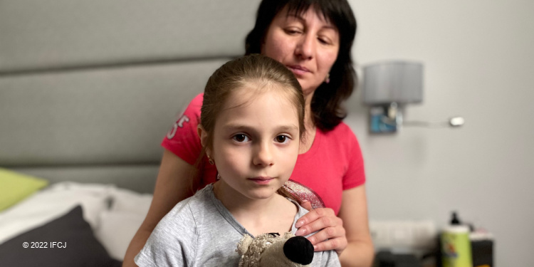 Young girl looking into the camera as her mother is behind her.