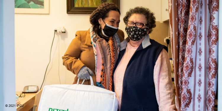 Yael Eckstein standing with an elderly Jewish woman while giving her an IFCJ branded blanket.