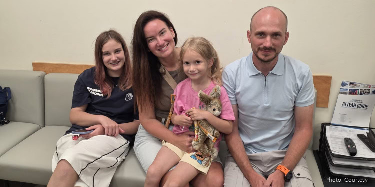A joyful family portrait featuring a mother, father, two young girls, and a small dog, sitting together on a sofa in a cozy indoor setting.