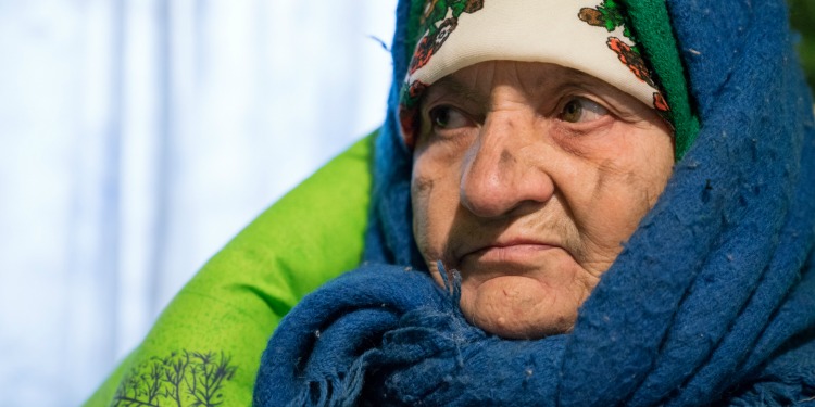 Elderly woman bundled up in scarves and blankets looking off into the distance.