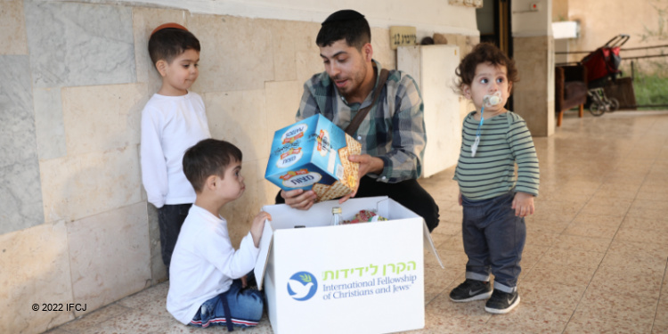 Dad looking at what's inside an IFCJ provided food box with his three sons.