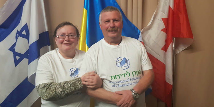 The podolskyi family in IFCJ shirts in front of flags.