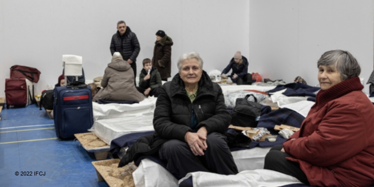 Elderly women sitting on cots in a refugee camp.