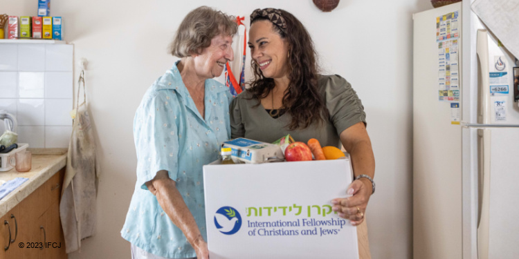 Elderly Jewish woman and Yael Eckstein smiling at each other while holding an IFCJ branded food box.