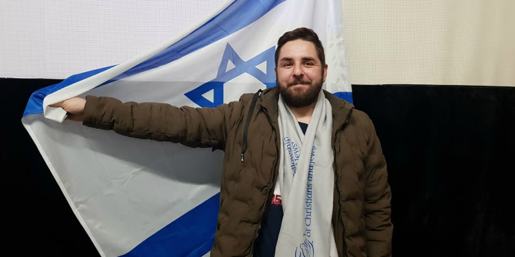 Man smiling into the Camera while wearing an IFCJ scarf and holding the Israeli flag.